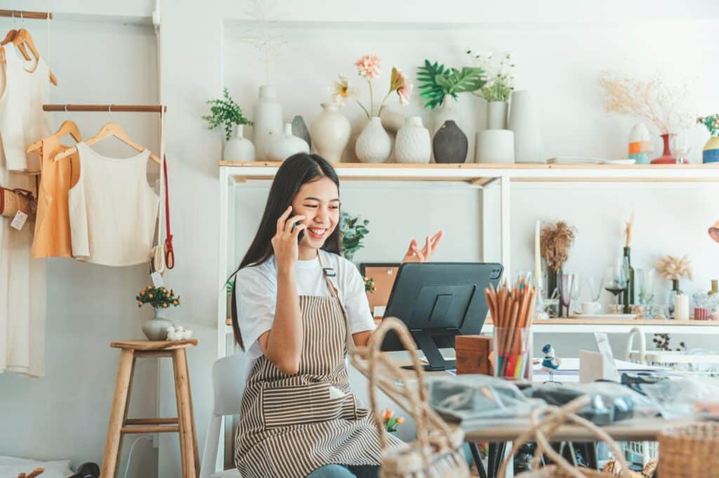 Small business owner talking on the phone with customers about features in a small shop.